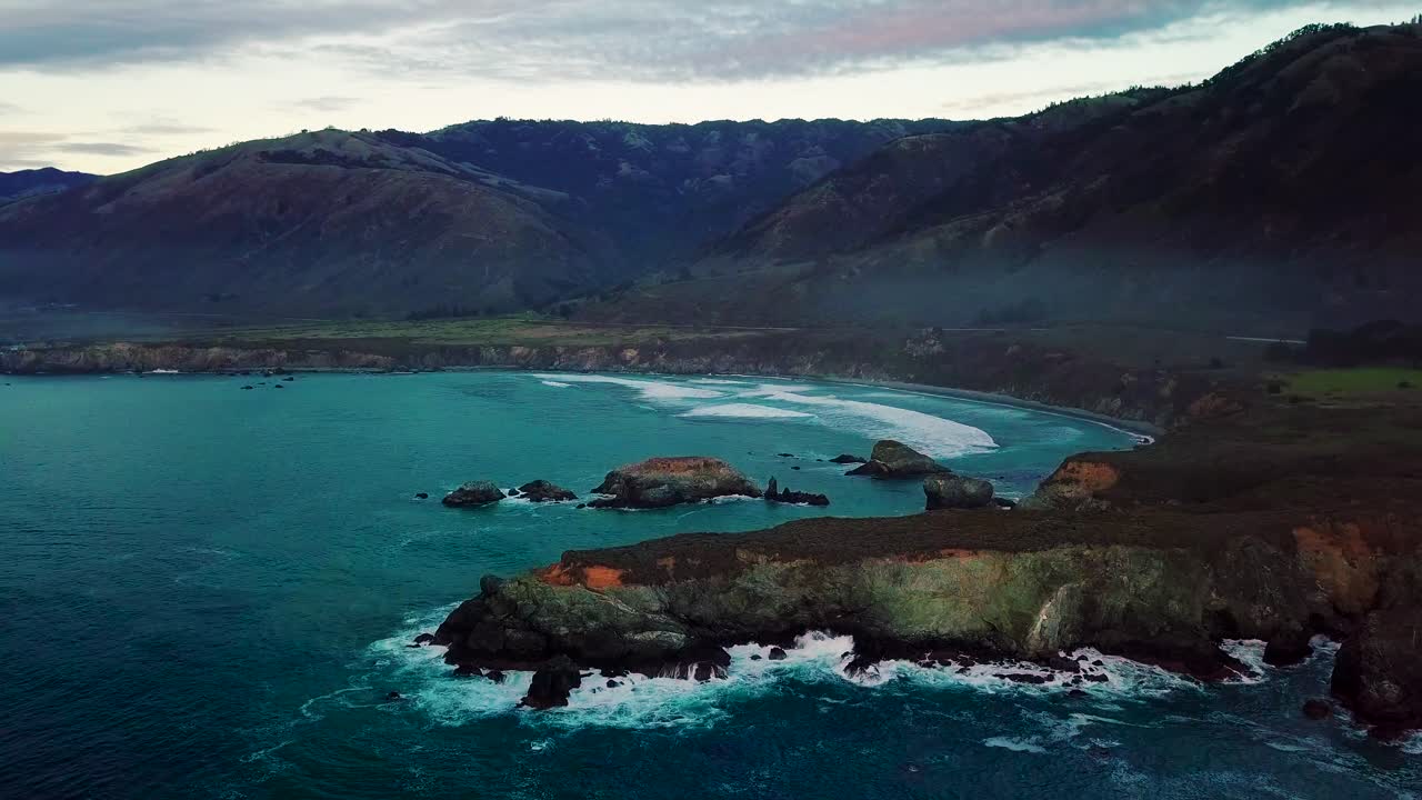 Ampia veduta aerea al crepuscolo di scogliere oceaniche e onde che si infrangono a Sand Dollar Beach, Big Sur, California