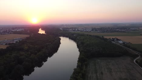 Drone-Aéreo-Sobre-Un-Hermoso-Río-Rodeado-De-Campos-De-Cultivo,-Puesta-De-Sol-Y-Agua