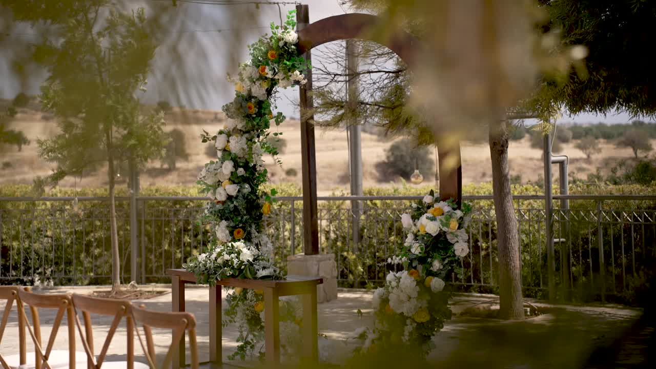 A charming wedding ceremony setup features a floral arch and wooden chairs in an open area surrounded by nature. The setting is perfect for a romantic celebration