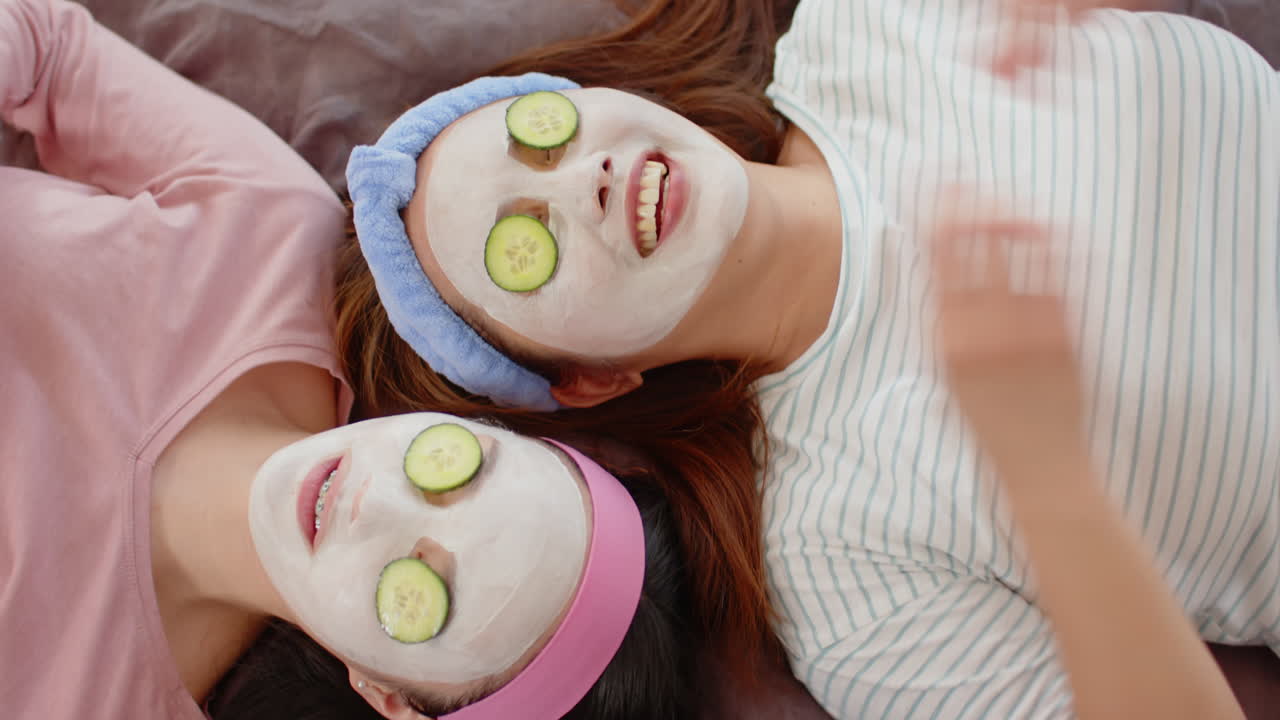 Applying face masks and placing cucumber slices, asian mother and child enjoying spa day