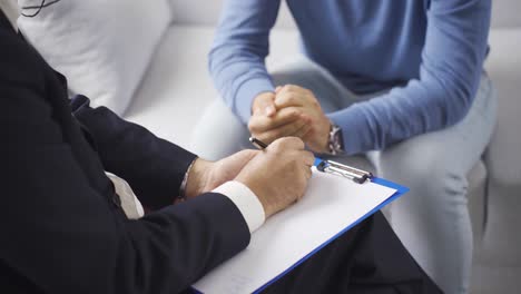 psychologist taking notes during therapy session with depressed male patient.