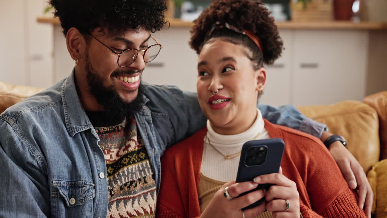 una pareja feliz riendo juntos en un sofá mientras miran un teléfono