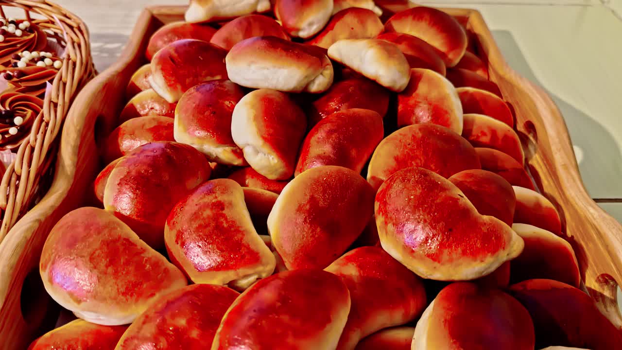 Handheld close up shot of glossy baked pastry buns piled in a wooden basket on a dessert table