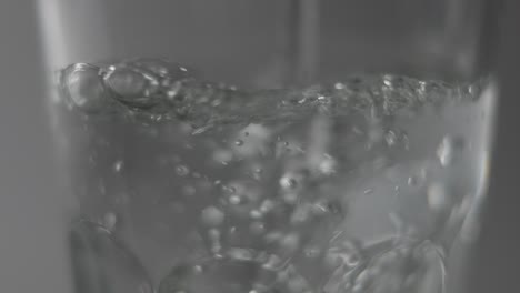 slowmotion macro of still water pouring into clear glass in front of dark background