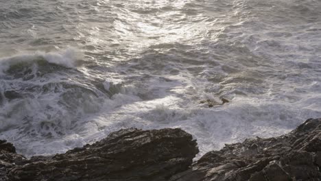 waves crash against rocky shores in nervi, genoa, with sunlight reflecting on the turbulent sea