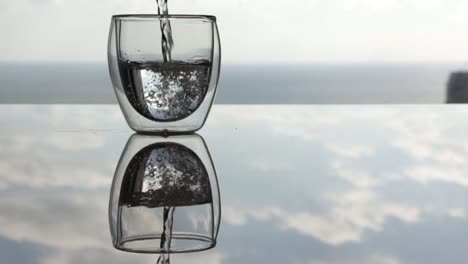 Pouring-water-in-a-glass-with-double-glass,-reflection-surface