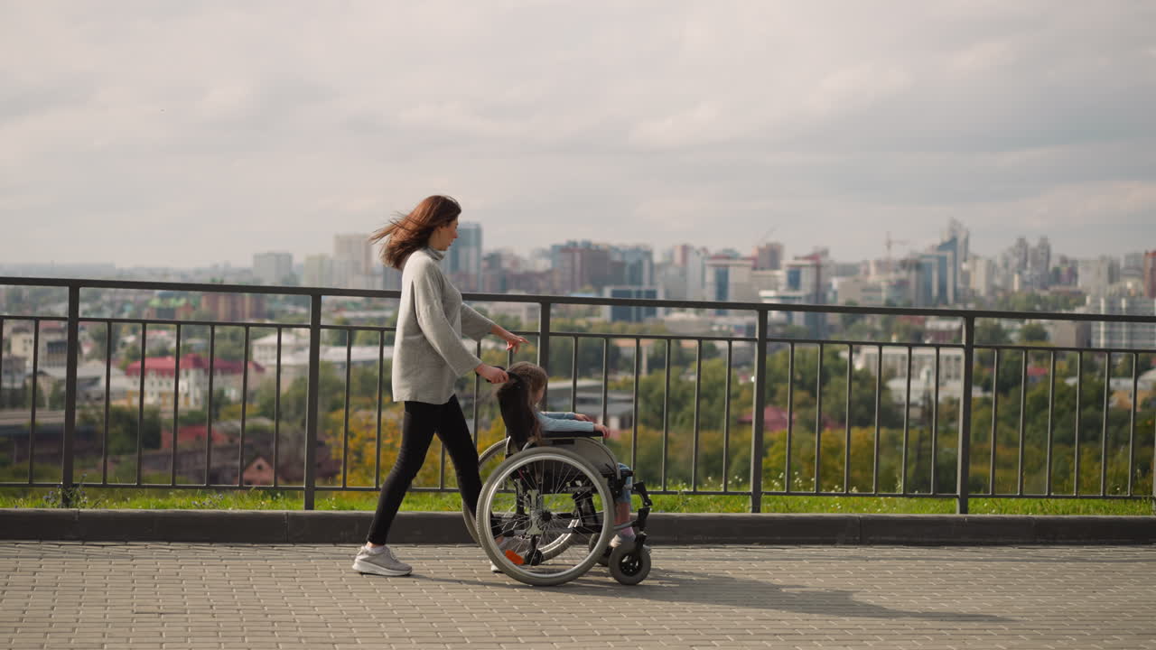 madre muestra panorama de la ciudad a la hija pequeña en silla de ruedas