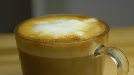 slow shallow focus slide shot of cup of hot cappuccino on wooden table