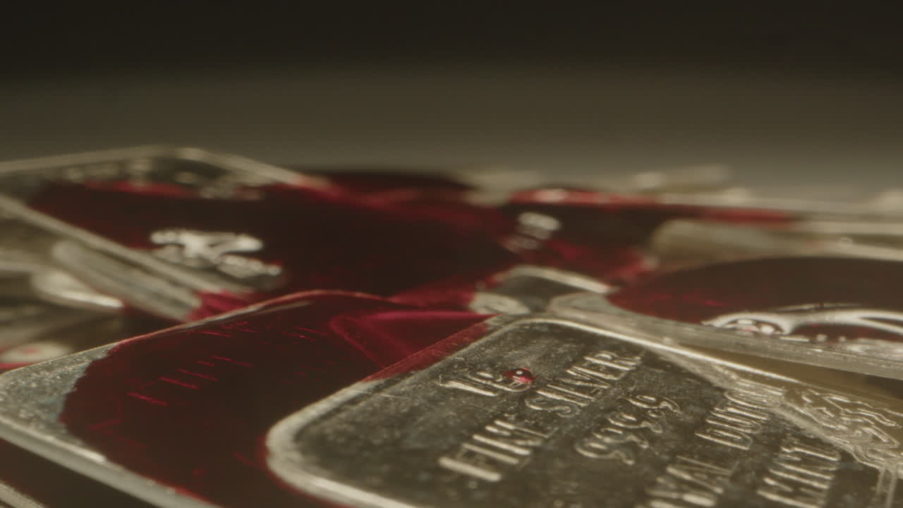 Extreme close up of blood dripping on silver bars. The blood slowly flows over the shiny precious metal plates