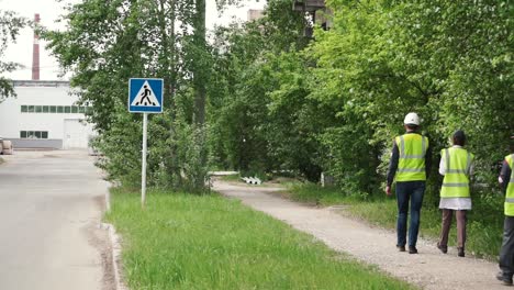 workers walking along a path near a factory with a crosswalk sign