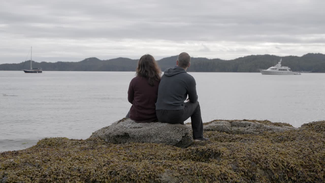 Couple watching salmon on rocky beach cloudy