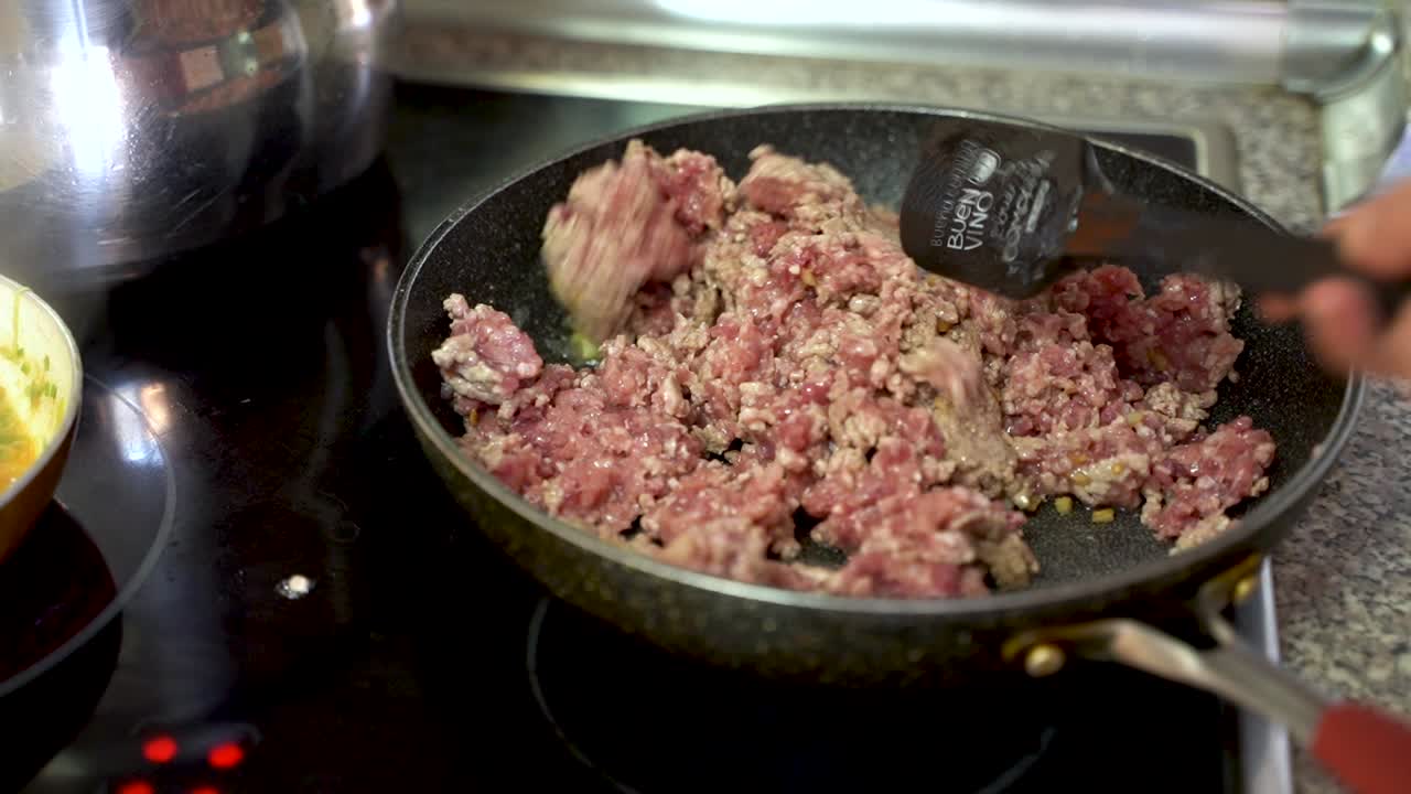 carne de cerdo molida chisporroteando en la sartén de la estufa