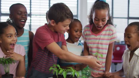 Diverse-group-of-happy-schoolchildren-looking-after-plants-in-classroom-during-nature-studies-lesson