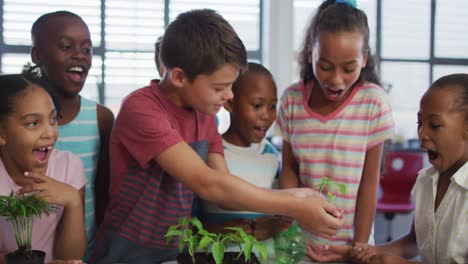 diverse group of happy schoolchildren looking after plants in classroom during nature studies lesson