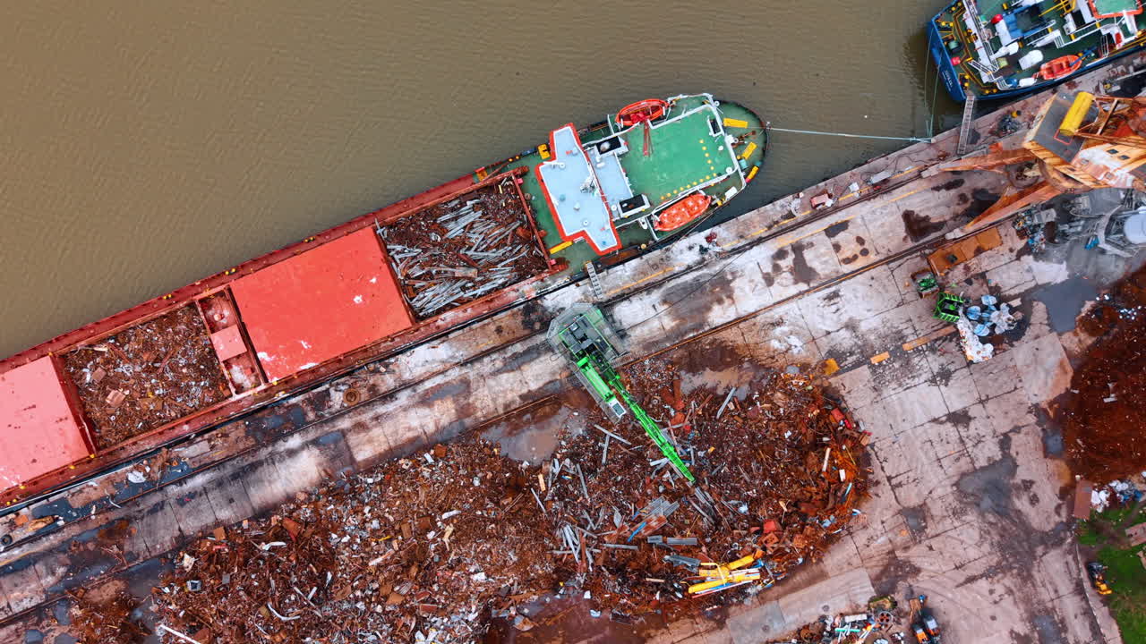 Vista dall'alto di una gru che carica rottami su una nave. Una gru idraulica verde sposta rottami metallici dal molo alla stiva di una nave da carico.