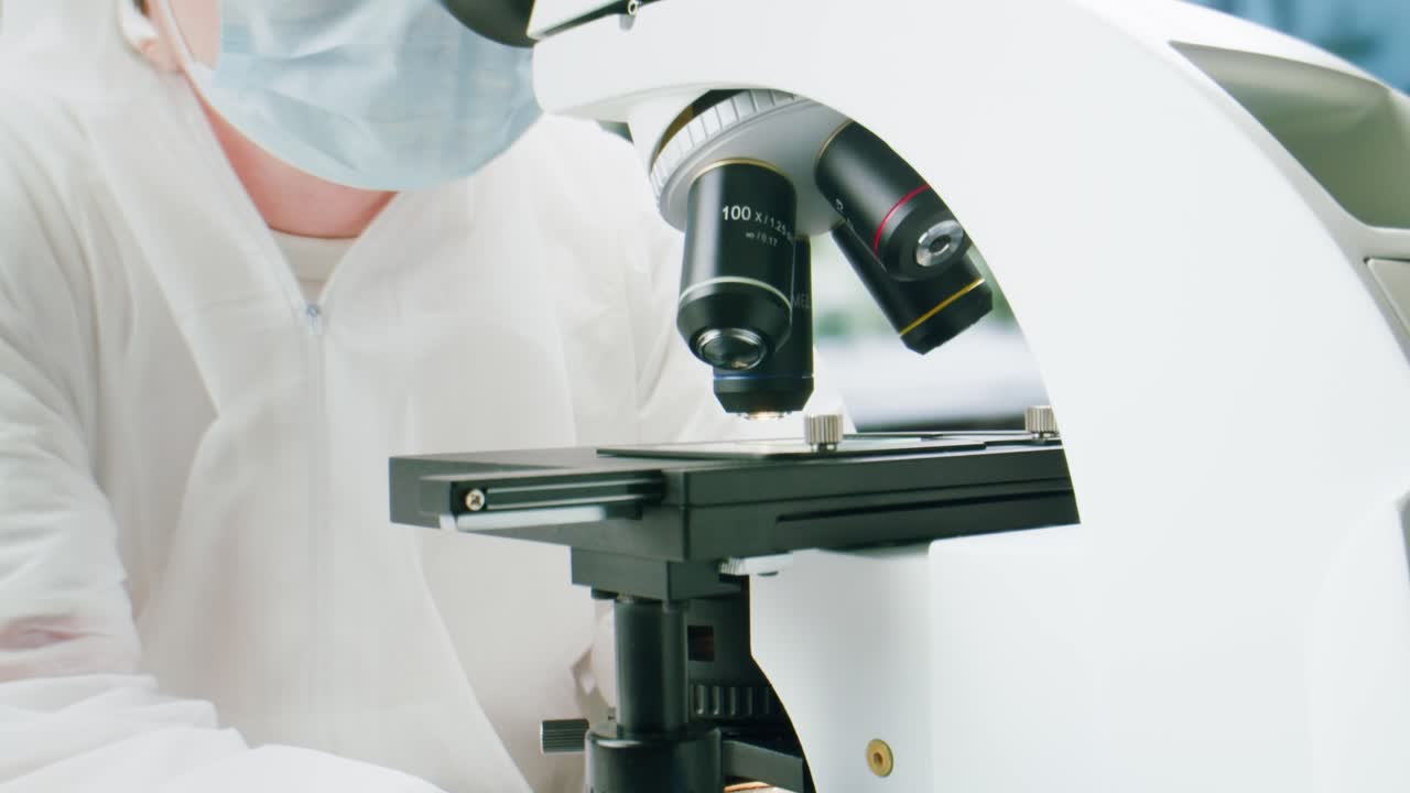 Scientist in Lab Coat Adjusting and Looking Through Microscope