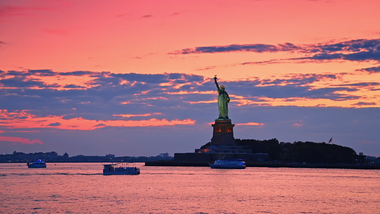 Sunset at statue of liberty. The Statue of Liberty stands tall against a vibrant sunset sky, boats gently gliding in the water nearby