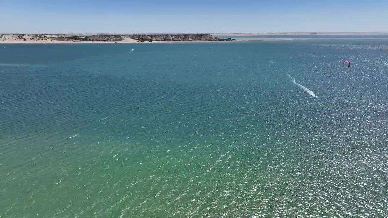 Güney Fas'taki Dakhla Lagünü'nün geniş sularının, uzaktaki kıyı şeridi ve açık kıyı manzarasıyla drone havadan görünümü. Seyahat ve belgesel projeleri için ideal, huzurlu doğal manzara.