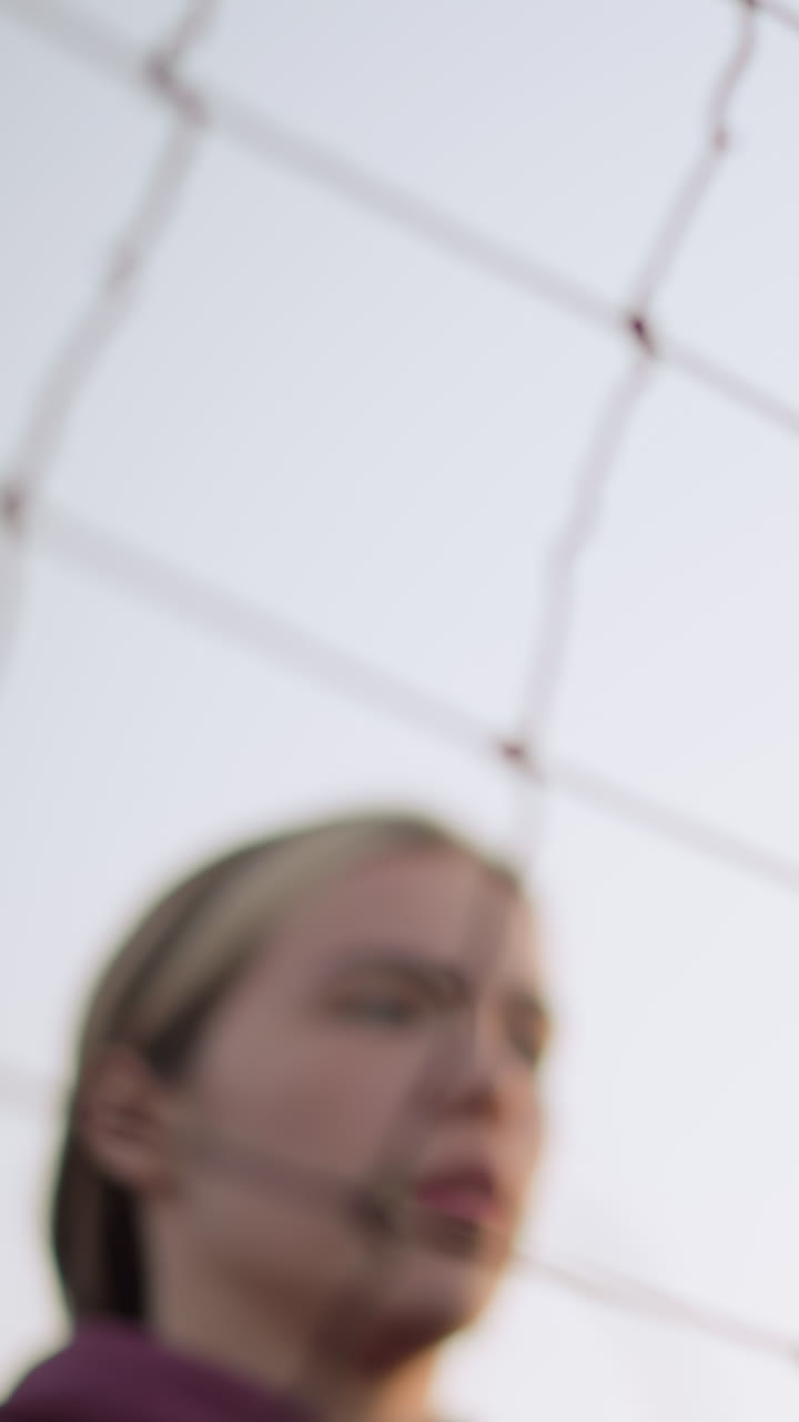 primer plano de una joven atleta que salta y juega voleibol, preparándose para golpear la pelota, la expresión enfocada muestra determinación y concentración, el fondo borroso presenta la red y los árboles