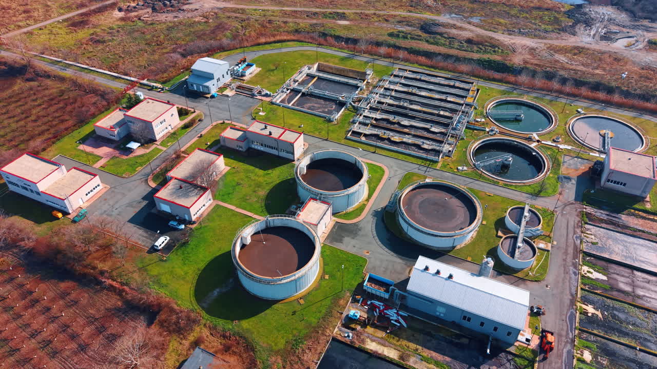 Aerial view of industrial water treatment complex with various tanks. Detailed shot of circular and rectangular processing units with red roof buildings