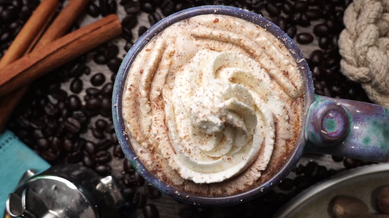 Cup or mug of coffee in a blue ceramic cup with whipped cream and a dash of nutmeg or cinnamon. Coffee beans surrounding a cozy cup of coffee in a blue mug.