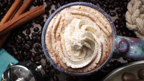 cup or mug of coffee in a blue ceramic cup with whipped cream and a dash of nutmeg or cinnamon. coffee beans surrounding a cozy cup of coffee in a blue mug.