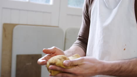 primer plano de un alfarero masculino con un delantal limpiando las manos con una esponja en un estudio de cerámica