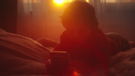 child playing smartphone in bed at sunrise/sunset