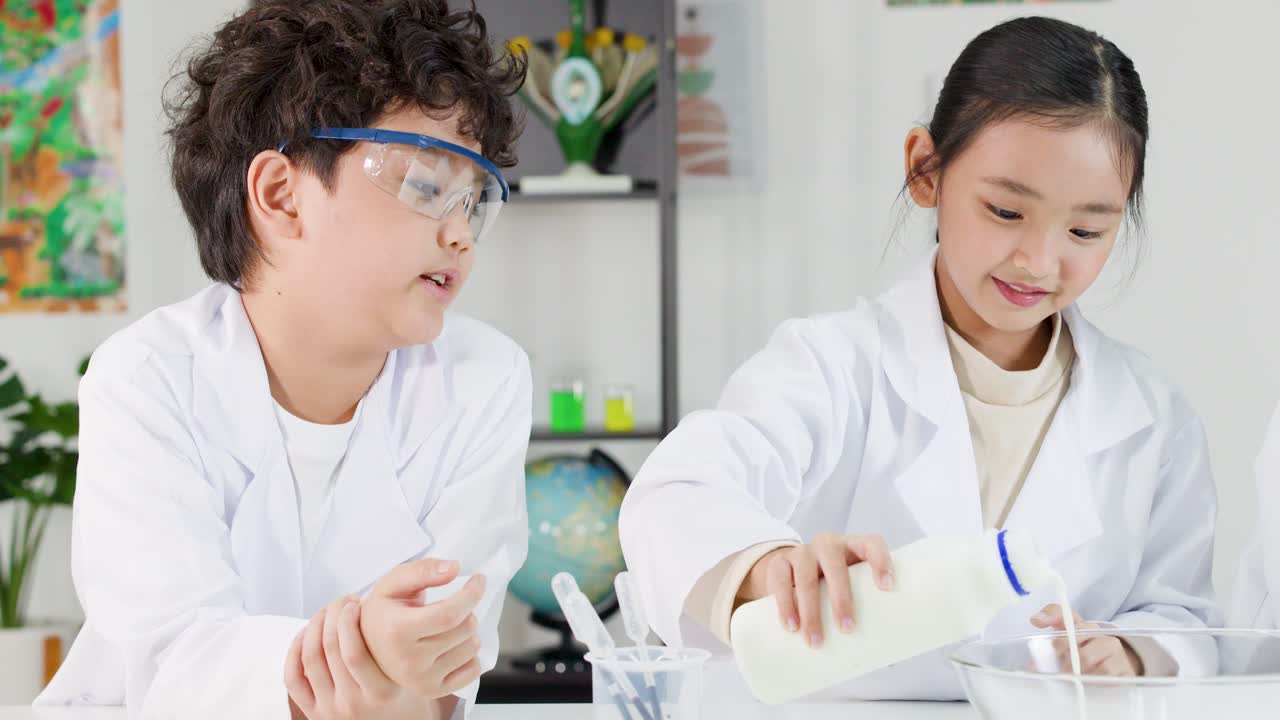 安全ゴーグルと白衣を着用した2人の若いアジア人学生が、ボウルに牛乳を注いでいる。