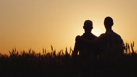 two gay men stand hugging at sunset looking forward to the horizon