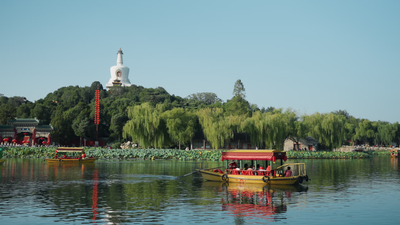 Du khách châu Á trên thuyền trên hồ tĩnh lặng ngắm bảo tháp trắng, bờ hồ rợp bóng liễu, chiếc thuyền du lịch màu vàng lướt nhẹ trên mặt nước phủ đầy sen, ánh nắng dịu nhẹ, những hình ảnh phản chiếu như gương, ngôi chùa xa xăm trên đồi, tất cả tạo nên một khung cảnh thanh bình và thong thả.