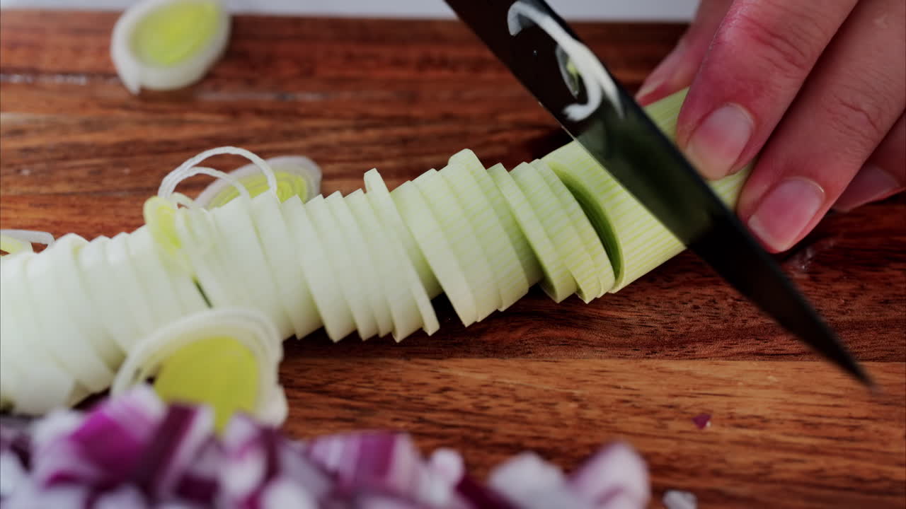 Woman cutting up leek near other vegetables on a wooden cutting board