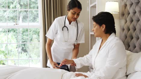 female doctor measuring blood pressure of mature woman in bedroom 4k