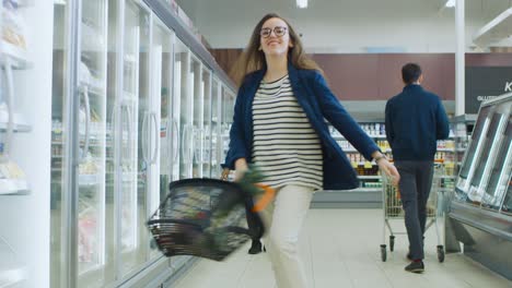 at the supermarket: happy young girl holding shopping basket dances through frozen goods and dairy products section of the store.