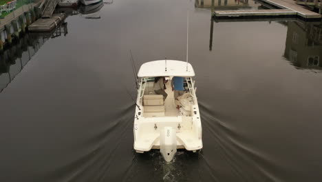 una vista aérea de un barco de pesca, navegando lentamente a través de un canal detrás de las casas en long island en un día nublado