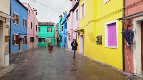 curious nosy woman examines burano colourful painted houses on wet day