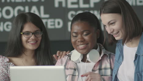 multicultural group of student girls laughing in front of a laptop