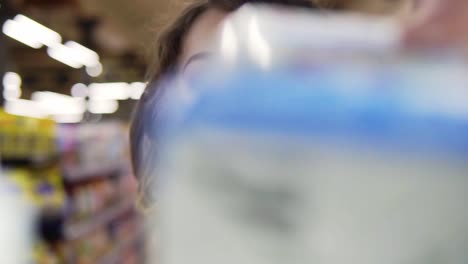 close up portrait of a young curly haired woman doing grocery shopping at the supermarket, she is reading a product label and