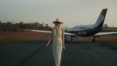 woman in elegant dress walking towards private jet at airport