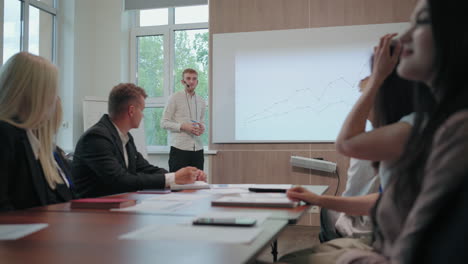 young professional it specialist is showing chart in meeting of board of directors and colleagues