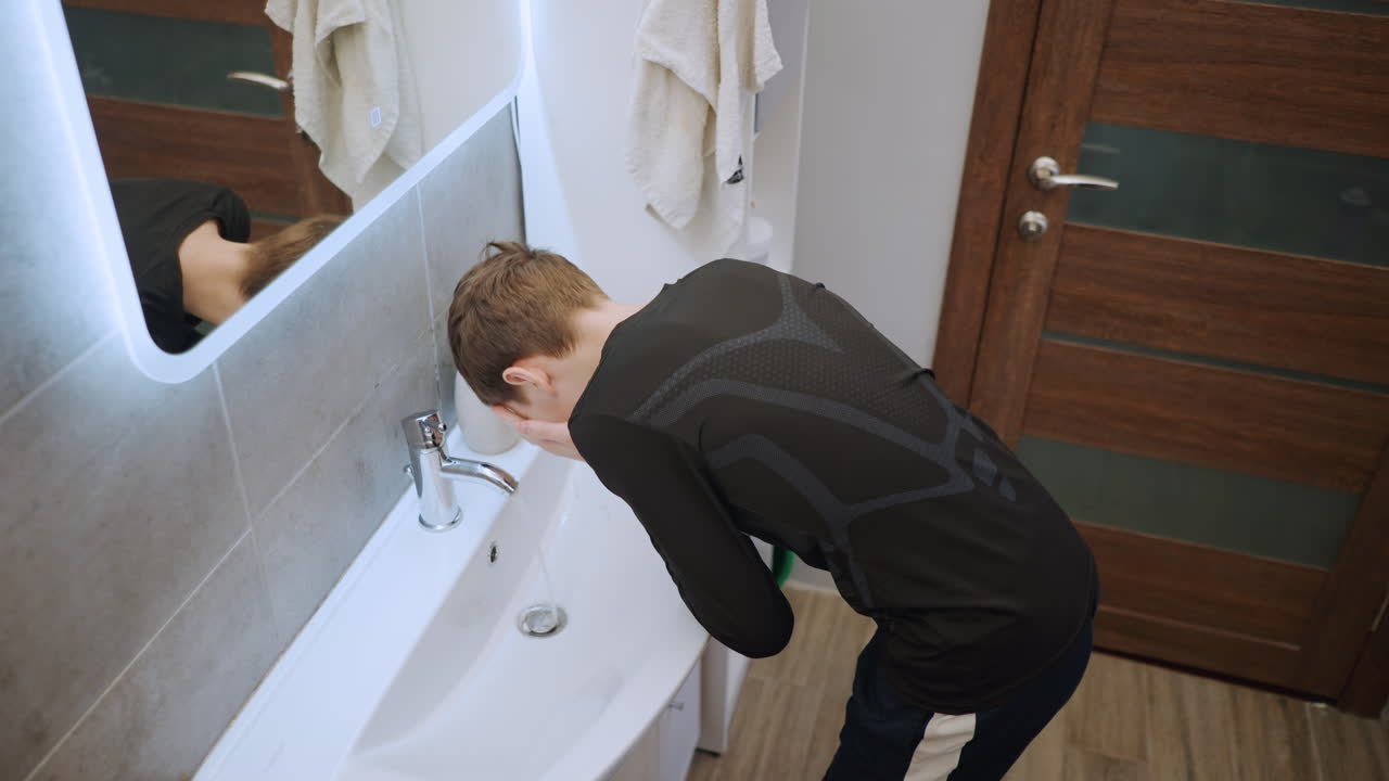 Boy freshens up in peaceful bathroom routine. Young boy performs calming nightly face wash at mirror. Child attentively participates in quiet evening hygiene routine before sleeping