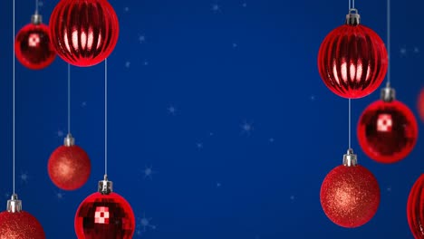 Animation-of-snow-falling-over-christmas-bauble-decorations-on-blue-background