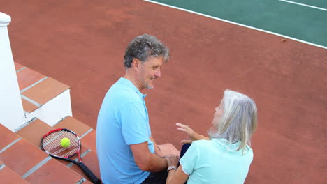 una pareja mayor sentada en las escaleras de la cancha de tenis 4k