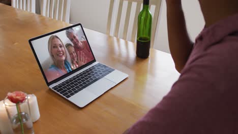 Mid-section-of-african-american-man-drinking-wine-while-having-a-video-call-on-laptop-at-home