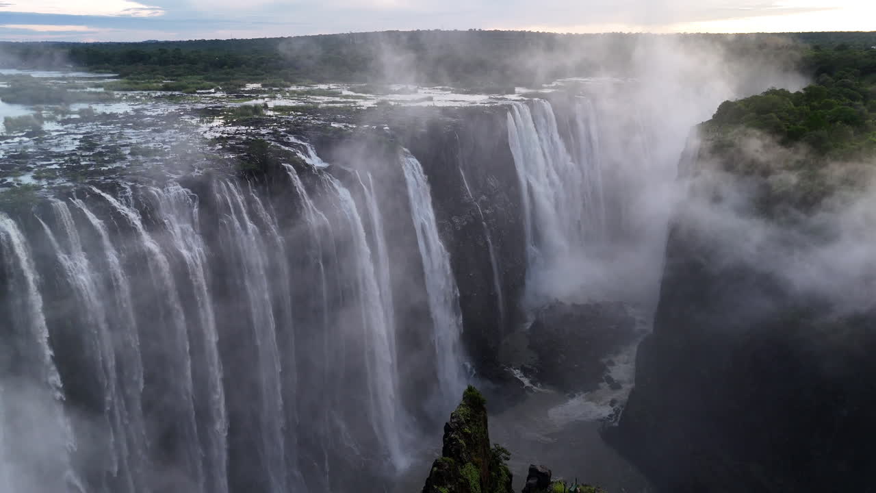 Aerial view of Victoria Falls with powerful waterfall plunging into gorge, mist rising above lush green forest, dramatic natural wonder and iconic travel destination in Africa