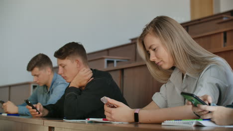 Un-Gran-Grupo-De-Hombres-Y-Mujeres-Se-Sientan-En-El-Auditorio-De-La-Universidad-Y-Miran-Vídeos-En-Internet-En-Teléfonos-Inteligentes,-Escriben-Mensajes-Y-Chatean-En-Línea.-Comportamiento-Antisocial-De-Los-Introvertidos.-El-Problema-Moderno-De-La-Sociedad.