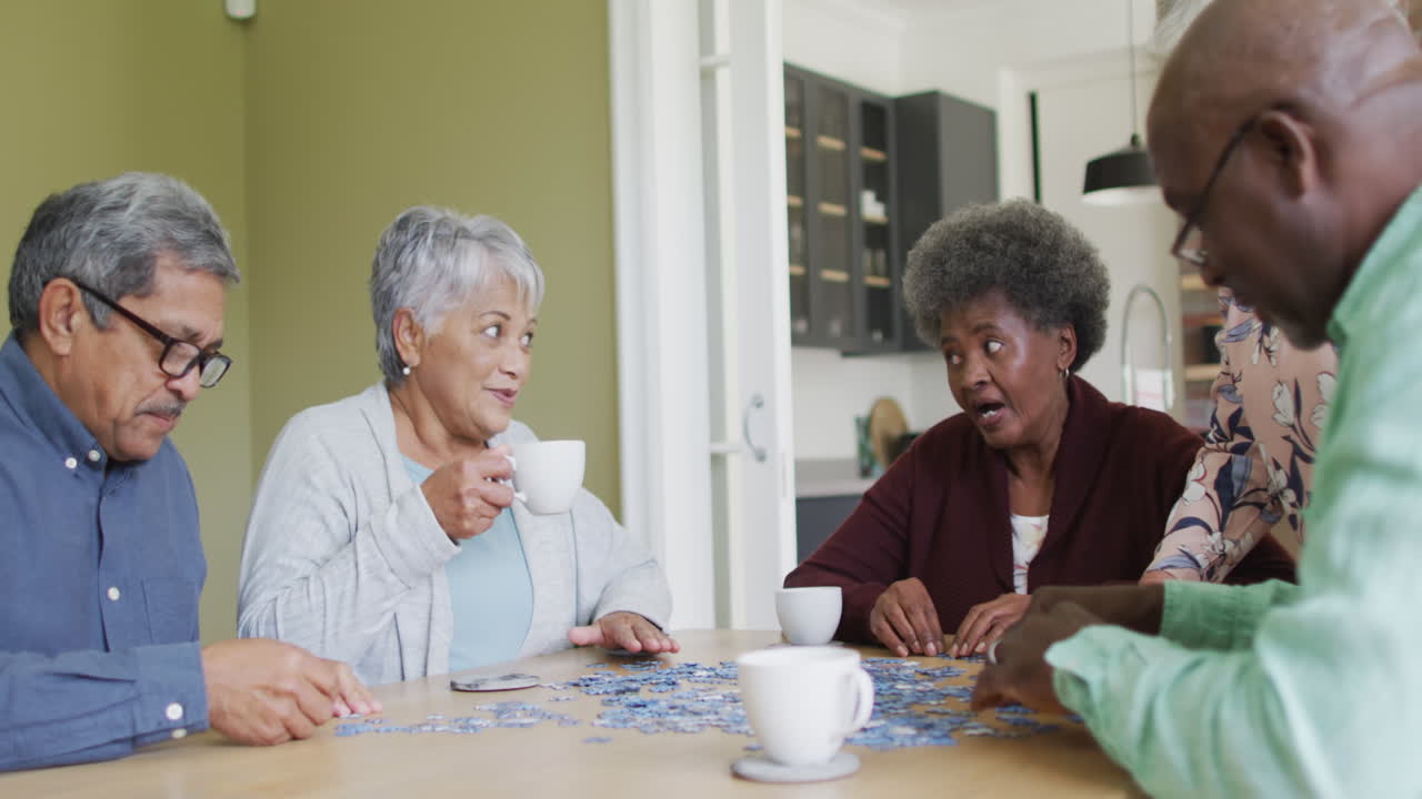 grupo de felices y diversos amigos mayores bebiendo café y haciendo rompecabezas en casa