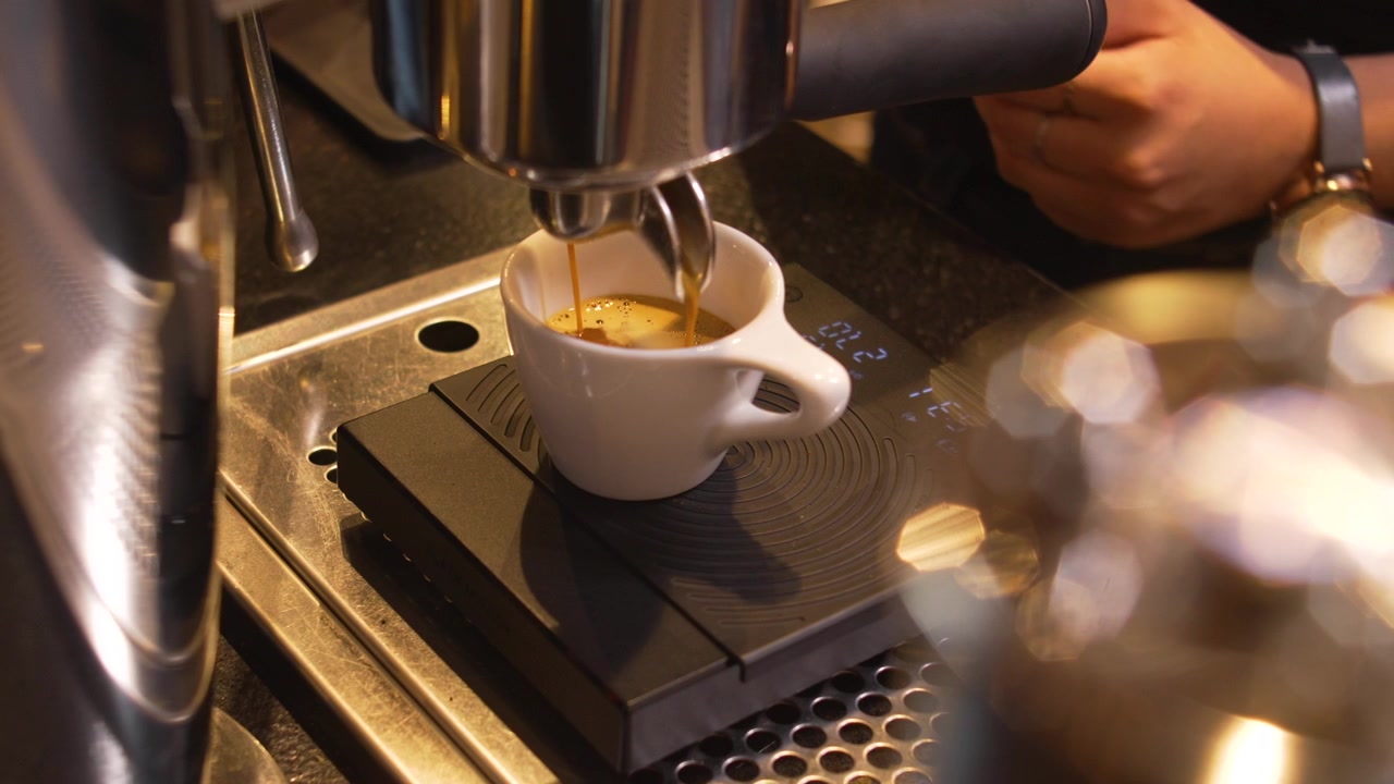 Erogazione di espresso di precisione in tazza bianca su bilancia digitale da una lussuosa macchina da caffè in acciaio inossidabile, atmosfera da caffetteria specializzata
