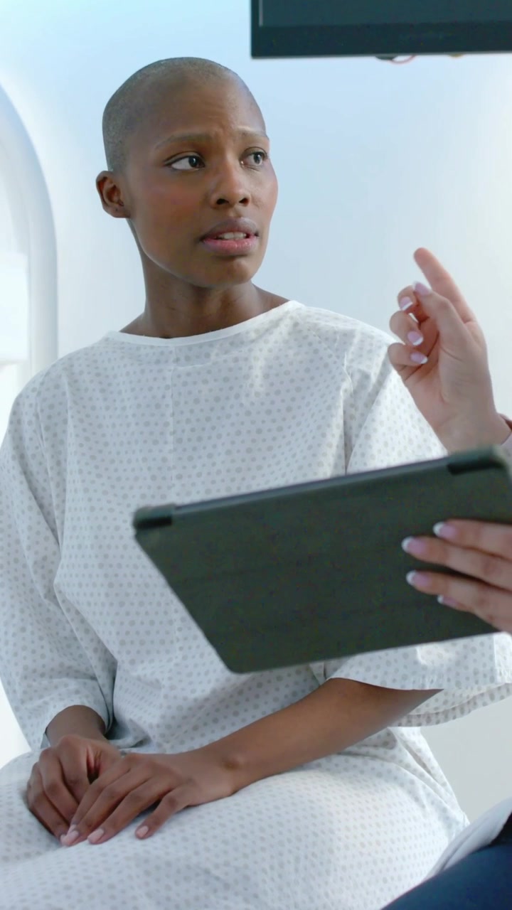 Vertical video: Listening woman reading tablet as doctor gesturing in exam table, reflecting, gown