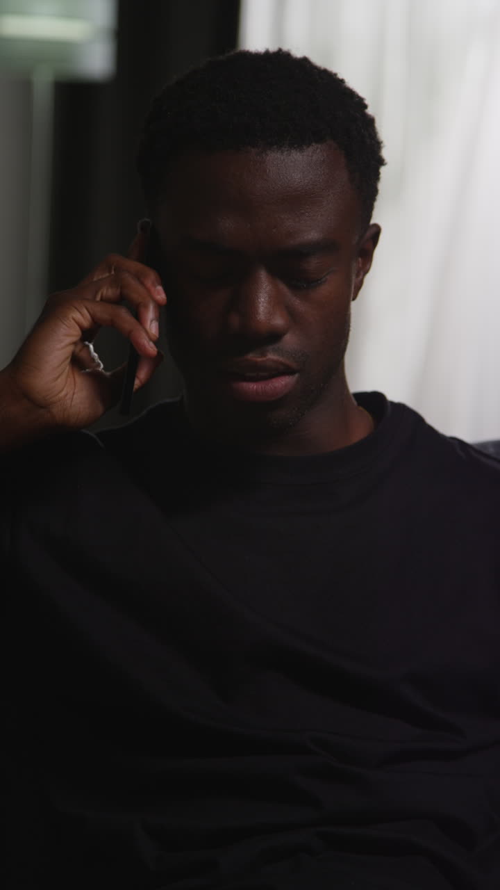 Vertical Video Of Unhappy And Depressed Young Man Sitting On Sofa At Home Talking On Mobile Phone